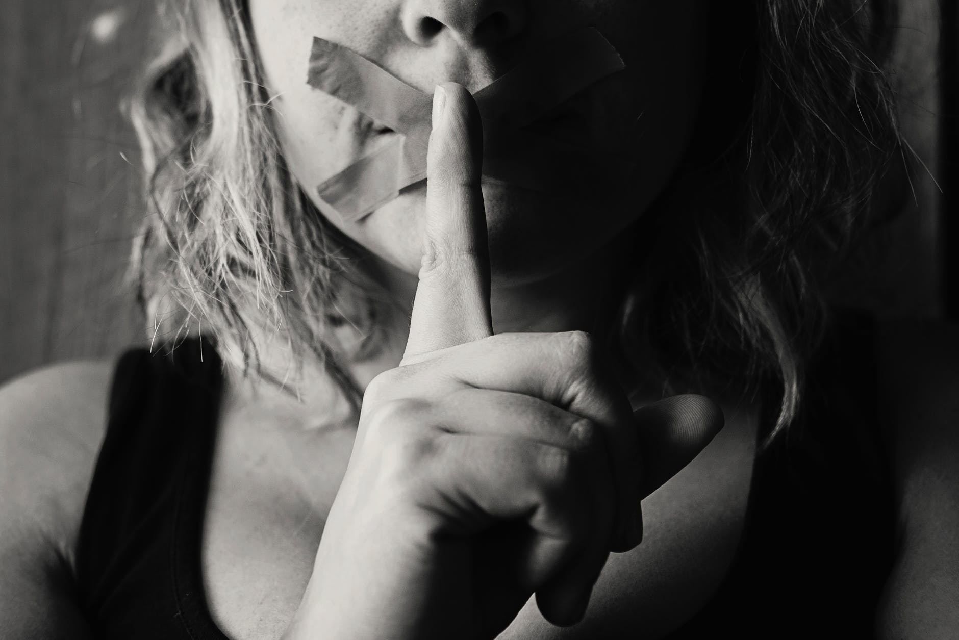 woman with tape over her mouth and finger to her mouth shushing