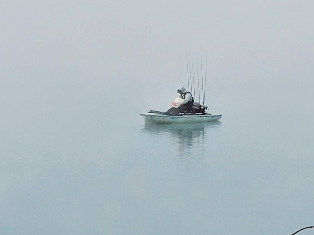 A lone fisherman out in a small boat with 7 fishing rods!