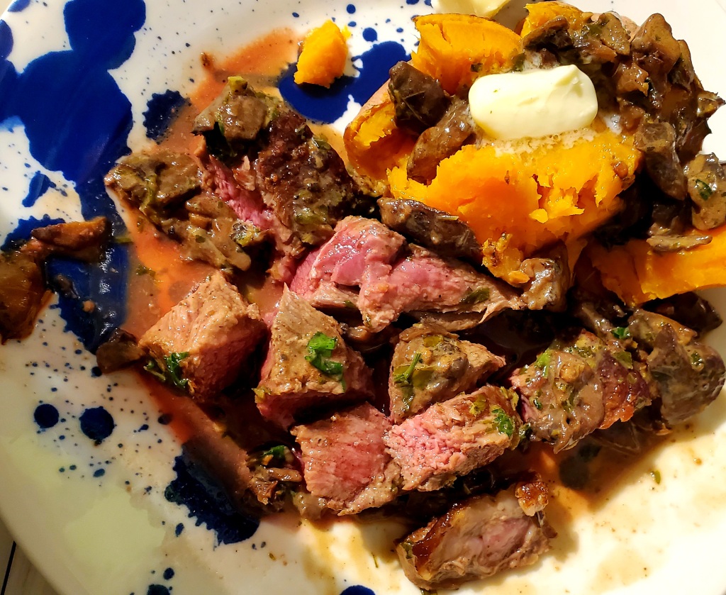 Steak cut up alongside buttered sweet potatoes